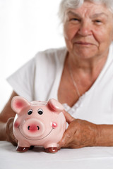 Elder woman holding and hugging funny pink piggybank. Budgeting expenses, making savings, effective investment concept. Future needs deposit. Focus on pig. Retirement and retiree finansial problems