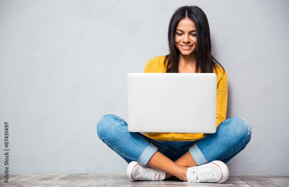 Wall mural Woman sitting on the floor and using laptop