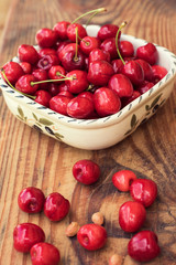 Ripe organic homegrown cherries and stones in a vintage ceramic bowl, on wooden background