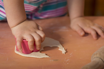 Little chef hands smeary with flour cutting the dough in flower shaped