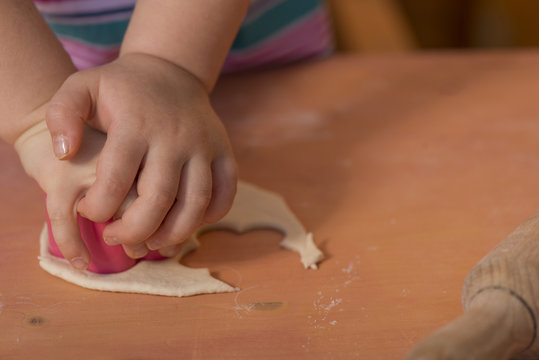 Little chef hands smeary with flour cutting the dough in flower shaped