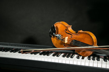 Piano keyboards with old violin on dark background.