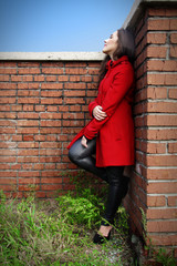 Beautiful woman in a red coat on a brick wall in the city