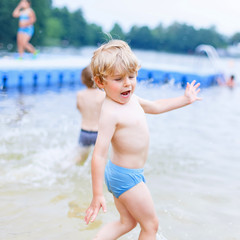 Little blond kid boy having fun with splashing in a lake, outdoo