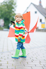 Little blond kid boy walking with big umbrella outdoors