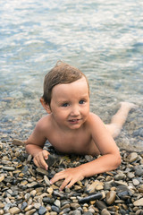 Fototapeta na wymiar Three year boy bathes in the sea on pebbles