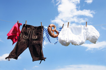 Oktoberfest, Volksfest - Lederhose, Dirndl und Breze hängen an Leine vor weiß-blauem Himmel,...