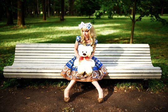 Portrait of young woman dressed as doll sitting on bench