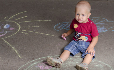 Naklejka premium little boy draws with chalk on the pavement sun