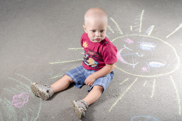 Naklejka premium little boy draws with chalk on the pavement sun