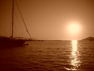 Summer sunset at sea with moored boat; monochrome. Image filtered in faded, washed out, retro style with sepia filter; nostalgic summer vintage concept.