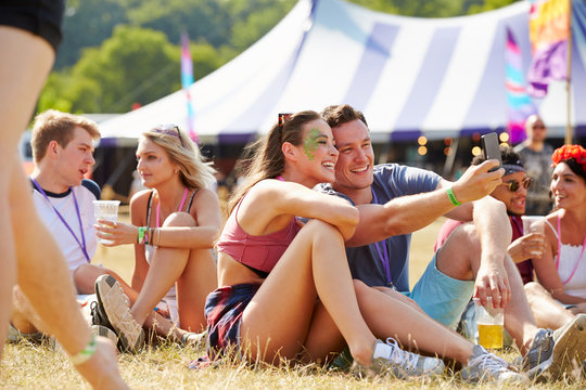 Friends sitting on the grass taking selfie at music festival