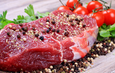 Raw beefsteak with spices and cherry tomatoes on wooden background