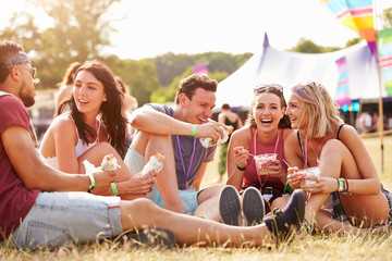 Friends sitting on the grass eating at a music festival - obrazy, fototapety, plakaty