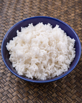 Cooked steamed rice in a blue bowl over wicker background