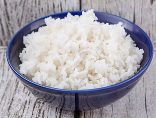 Cooked steamed rice in a blue bowl over wooden background