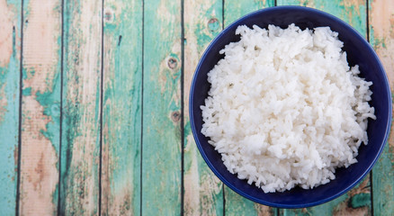 Cooked steamed rice in a blue bowl over wooden background