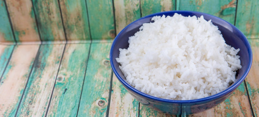 Cooked steamed rice in a blue bowl over wooden background