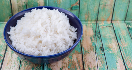 Cooked steamed rice in a blue bowl over wooden background
