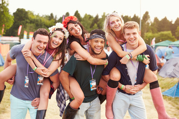 Friends giving piggy backs through music festival campsite
