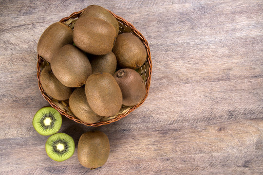 Some kiwis in a basket over a wooden surface