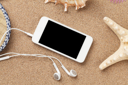 Smartphone on sea sand with starfish and shells
