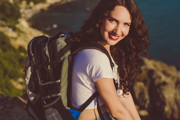 Obraz na płótnie Canvas Happy girl with backpack is sitting on rock peak 