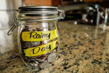 Rainy Day Money Jar. A clear glass jar filed with coins and bills, saving money. The words 