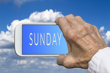 Smart phone in old hand with days of the week - Sunday on screen