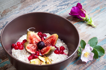 Home made bircher style muesli porridge topped with fresh sliced fig, pomegranate seeds, pistachio nuts coconut,chia seeds and a cherry. Served on a rustic wooden table.