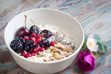 Healthy home made oatmeal porridge muesli with kefir yogurt and topped with blackberries, cherries,pomegranate, pumpkin and chia seeds. Served on a rustic wooden table.