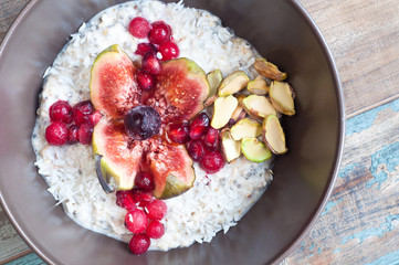 Home made bircher style muesli porridge topped with fresh sliced fig, pomegranate seeds, pistachio nuts coconut,chia seeds and a cherry. Served on a rustic wooden table.