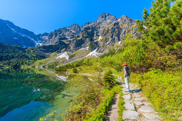 Fototapeta na wymiar Woman tourist standing on path along beautiful green water Morskie Oko lake, Tatra Mountains, Poland
