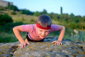 Young boy doing push-ups on a rock