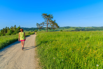 Young woman tourist walking on rural road along green meadow in Tatra Mountains, Poland