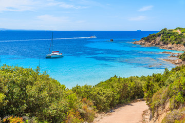 Path to Grande Sperone beach with catamaran boat on sea in distance, Corsica island, France
