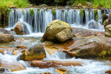 Waterfall on a mountain river with rock and forest in background