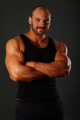 Fototapeta premium Portrait of muscular man in black shirt standing on gray background