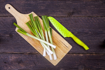 Scallions bunch cleaned and prepared on a wooden board and chopping board with a knife next to it