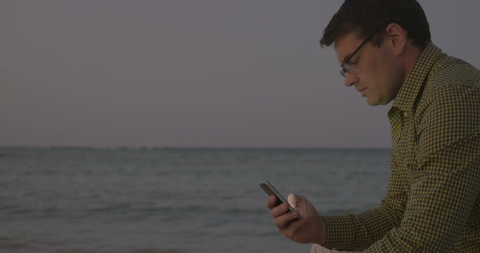 Young man using smart phone by sea in the evening