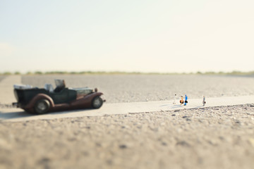 Fototapeta na wymiar four travelers(miniature) and a classic car on country road.Shallow depth of field composition and soft pastel style.