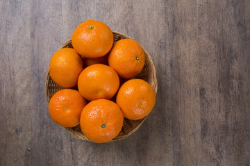 Some tangerines in a basket over a wooden surface