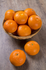 Some tangerines in a basket over a wooden surface