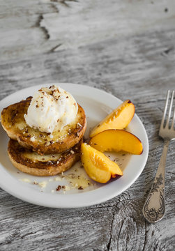 French toast with vanilla ice cream, honey, nuts and peaches on a white plate on a light wooden background