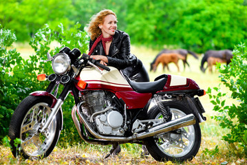Naklejka na ściany i meble Biker girl in leather jacket on a motorcycle against the