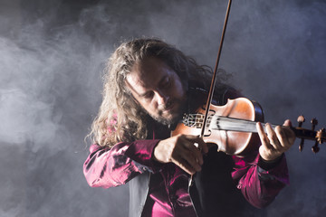 handsome man playing classical violin through blue smoke
