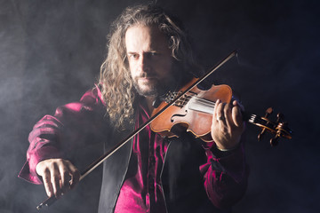 handsome man playing classical violin through blue smoke