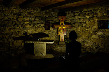 Betende Frau in der Kirche  a woman sits praying in a dark chapel in front of the cross with jesus