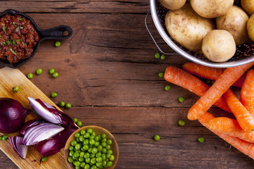 Sheperds pie ingredients with mince meat in a rustic pan shot on a wooden background from above