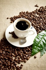 Wave diagonally made of coffee beans with cup of frothy coffee with leaf